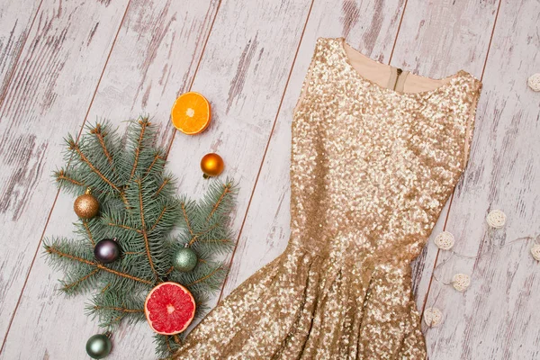 Vestido dourado com lantejoulas em um fundo de madeira, ramo de abeto e bolas e citrinos — Fotografia de Stock