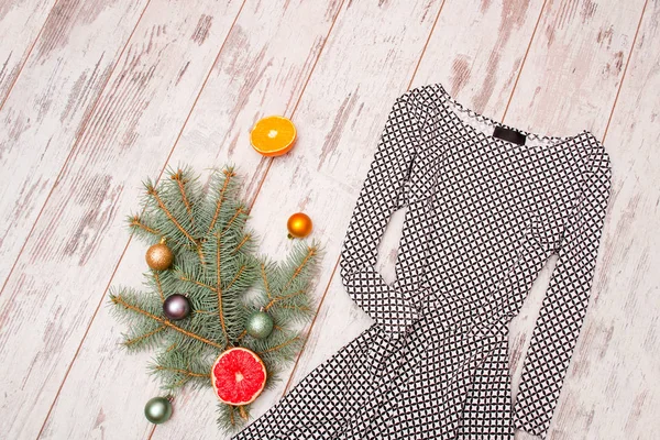 Dress in rhombuses on a wooden background, fur-tree branch with ornaments and citrus. View from above — Stock Photo, Image