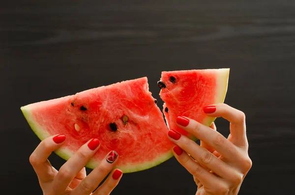 Grote segment van rijpe watermeloen in vrouwelijke handen op een zwarte achtergrond, gebroken close-up — Stockfoto