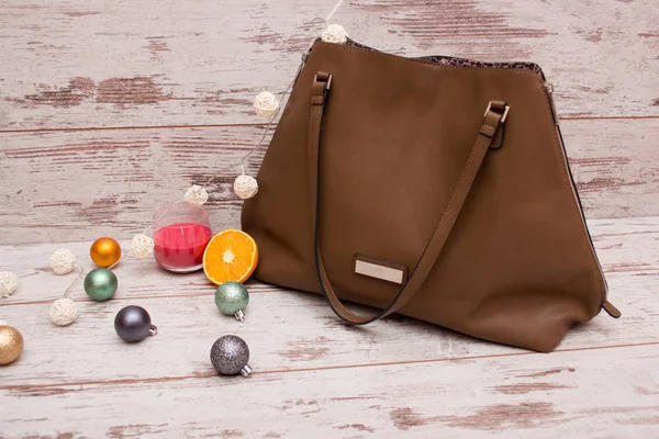 Big brown ladies handbag on a wooden background, Christmas ornaments, garland and candle. fashion concept