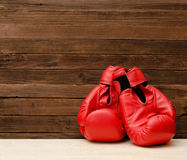 Dos guantes de boxeo rojos en un lado del marco sobre un fondo marrón de madera, espacio vacío — Foto de Stock