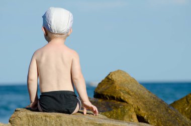 Küçük çocuk yüzme gövdeleri, mavi gökyüzü, metin için yer deniz kıyısına sırtında bir rock ile oturan