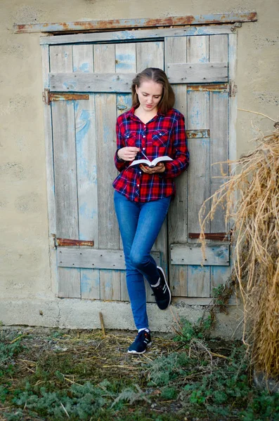 Girl in a plaid shirt and jeans reading a book, with his back to the door