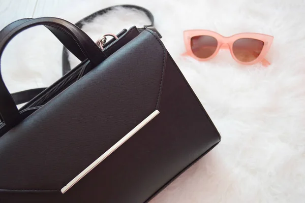 Черная сумочка и розовые очки на белом фоне. Концепция моды. вид сверху — стоковое фото