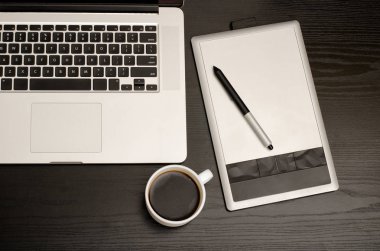 Grafik tablet kalem, laptop klavye, ve kahve siyah ahşap masa üzerinde kapat