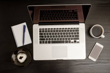 Siyah ahşap bir masa üzerinde bir dizüstü bilgisayar klavye, kahve kupa, bir akıllı telefon, bir dizüstü bilgisayar ve bir tatlı Üstten Görünüm