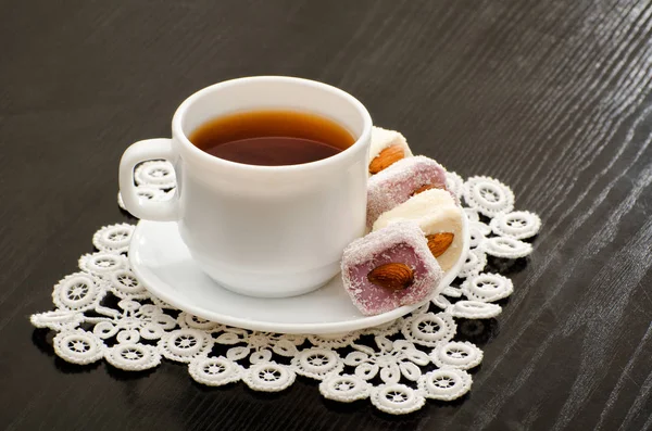 Mug of tea and Turkish delight with nuts on a plate, close-up, black background — Stock Photo, Image