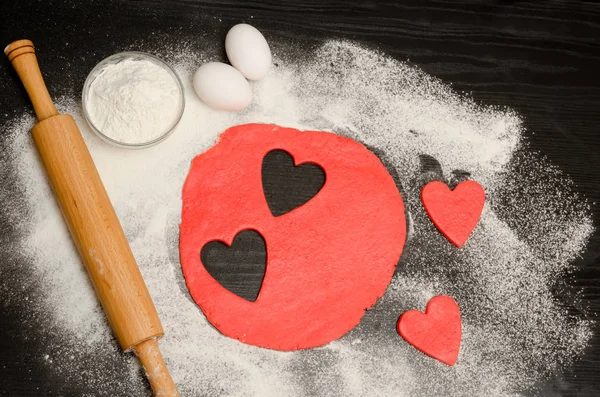 Hamuru oklava, yumurta ve un siyah bir tablo ile kırmızı kalpler kesip. Yukarıdan görüntüleyin. Metin için yer — Stok fotoğraf