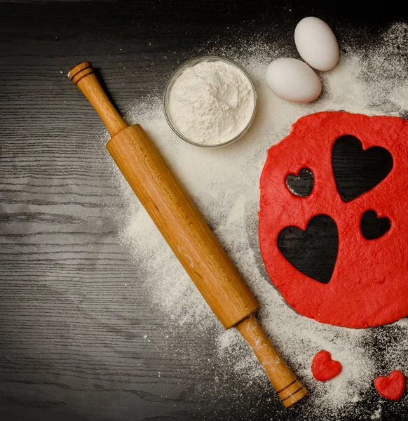 Coeurs rouges couper la pâte avec des œufs et de la farine sur une table noire, un rouleau à pâtisserie. Vue d'en haut. Espace pour le texte — Photo