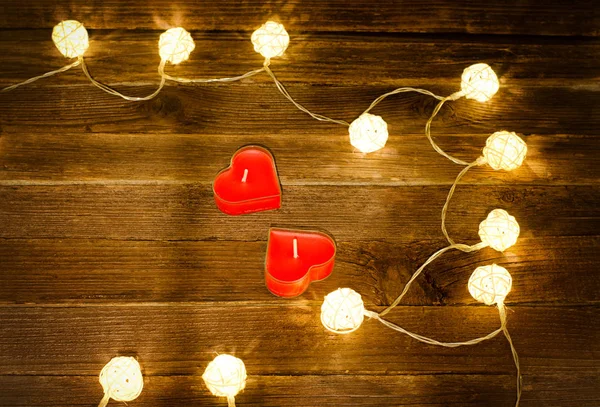 Duas velas vermelhas na forma de um coração e lanternas brilhantes feitas de vime em um fundo de madeira. Vista superior, espaço para texto — Fotografia de Stock