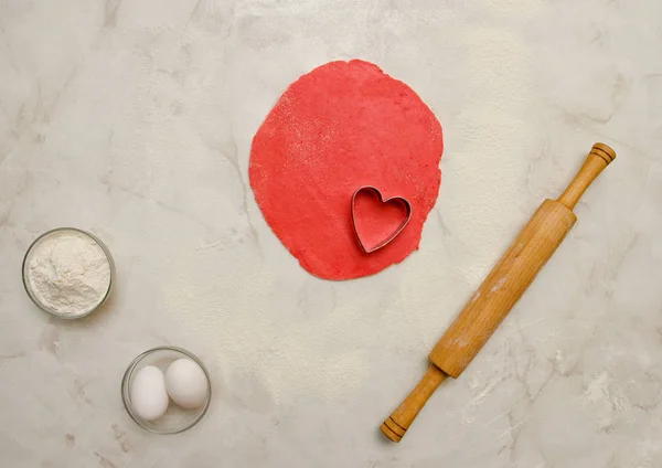 Kırmızı hamur kalp, oklava, yumurta ve un beyaz bir tablo dışarı bir kesim ile. Üstten Görünüm, metin için yer — Stok fotoğraf