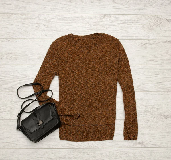 Brown-black sweater and black bag on a wooden background. Fashion concept. top view