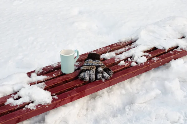 Guantes de mujer y azul una taza en un banco entre la nieve. Nadie en un marco —  Fotos de Stock