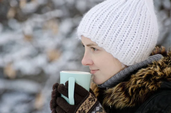 Chica en un sombrero blanco en invierno con taza de té, vista lateral, primer plano —  Fotos de Stock