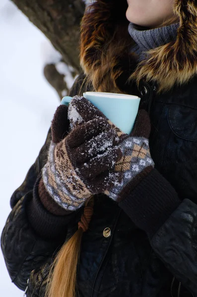 Дівчина в рукавичках обійняла чашку чаю, білий засніжений фон, обличчя не видно — стокове фото
