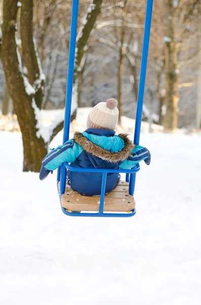 Kleine jongen zit op een schommel, prima weer winterdag achteraanzicht — Stockfoto