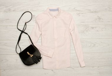 Hafif pembe gömlek ve siyah bir çanta. Ahşap arka plan. Moda kavramı, üstten görünüm