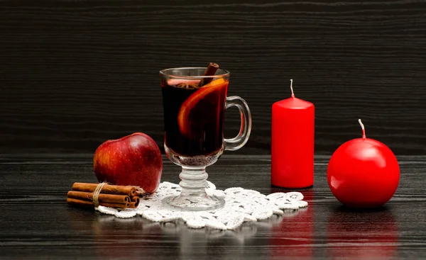 Vinho amassado com temperos em um guardanapo de cadarço. Velas vermelhas, paus de canela e maçã. Fundo de madeira preta — Fotografia de Stock