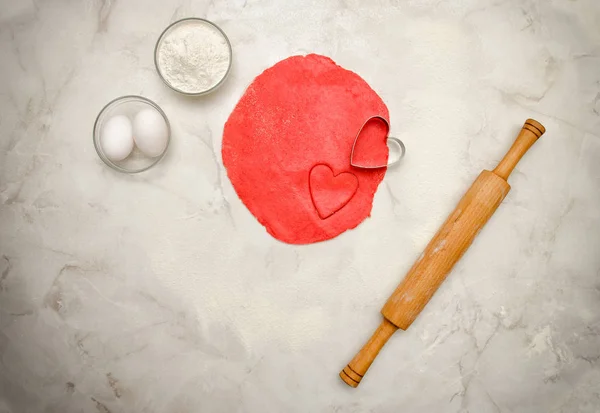 Kırmızı hamur kalp, oklava, yumurta ve un beyaz bir tablo dışarı bir kesim ile. Üstten Görünüm, metin için yer — Stok fotoğraf