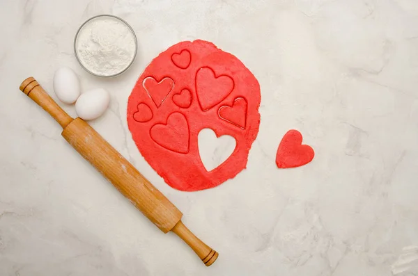 Bir oklava ve beyaz bir tabloda, üstten görünüm kalpleri dışarı kesim ile kırmızı hamur — Stok fotoğraf