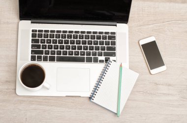 Bir fincan kahve ve bir not defteri açık bir laptop, smartphone. Hafif ahşap arka plan, üstten görünüm