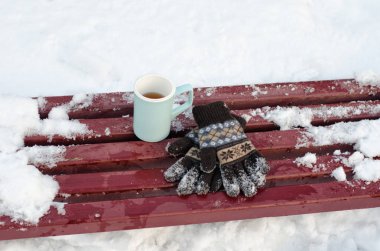 Mavi kupa çay ve kadın örme eldiven kışın, kar içinde belgili tanımlık geçmiş bir bankta. Yakın çekim