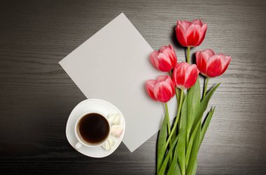 Beyaz boş bir kağıt yaprağına, pembe laleler ve bir fincan kahve. Siyah tablo. Üstten Görünüm