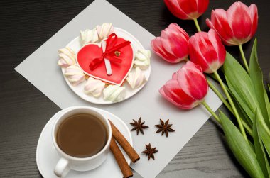 Gingerbread kalp şeklinde pembe laleler ve bir fincan kahve. Siyah tablo. Üstten Görünüm