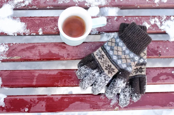 Kubek herbaty i damskie dziane rękawice na ławce w zimie śnieg poniżej. Widok z góry — Zdjęcie stockowe