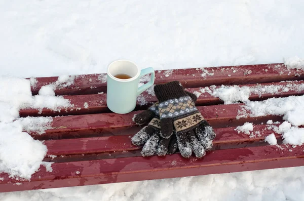Taza azul té y guantes de punto de las mujeres en un banco en el invierno, nieve en el fondo. Primer plano —  Fotos de Stock