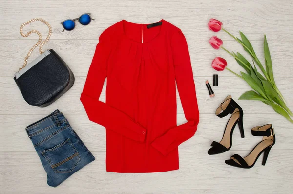 Concept de mode. Chemisier rouge, jeans, sac à main, lunettes de soleil, chaussures noires, rouge à lèvres et tulipes roses. Vue de dessus, fond bois clair — Photo