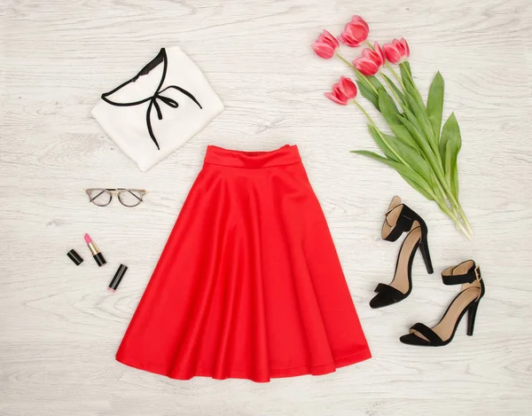Concetto moda. Gonna rossa, camicia, occhiali da sole, rossetto, scarpe nere e tulipani rosa. Vista dall'alto, fondo in legno chiaro — Foto Stock