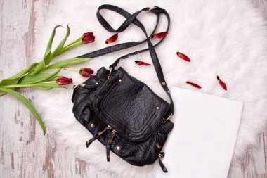 Siyah çanta, kağıt ve solmuş Lale beyaz kürk üzerinde beyaz bir levha. Moda kavramı, üstten görünüm