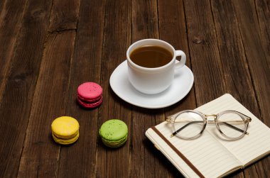 Kahve kupa, macarons, defter ve ahşap bir masa üzerinde gözlük. Yan görünüm