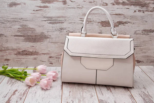 White bag with a handle on a wooden background, pink tulips. Fashionable concept.