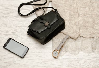 Siyah çanta, izle ve bej bir hırka üstünde hareket eden telefon. Moda kavramı, üstten görünüm