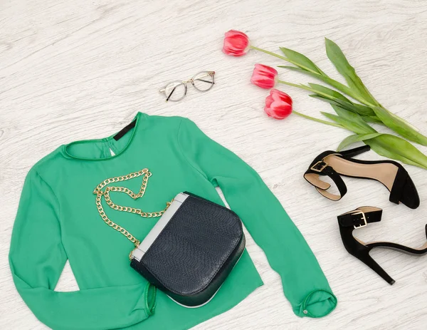 Fashion concept. Groene blouse, handtas, zonnebril, zwarte schoenen en roze tulpen. Bovenaanzicht — Stockfoto