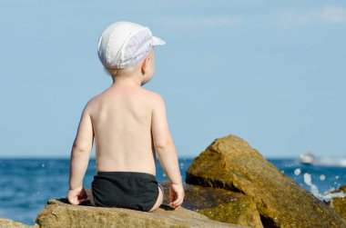 Küçük çocuk yüzme gövdeleri, mavi gökyüzü, metin için yer deniz kıyısına sırtında bir rock ile oturan