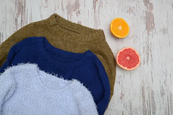 Três camisola quente em um fundo de madeira. Laranja e toranja. Conceito na moda, vista superior — Fotografia de Stock