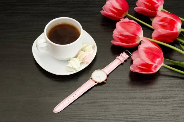 Taza con café y malvavisco, reloj, tulipanes rosados. Mesa negra. Vista superior —  Fotos de Stock