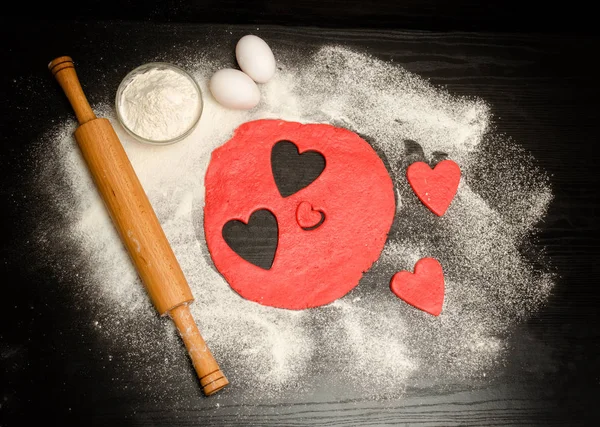 Hamuru oklava, yumurta ve un siyah bir tablo ile kırmızı kalpler kesip. Yukarıdan görüntüleyin. Metin için yer — Stok fotoğraf