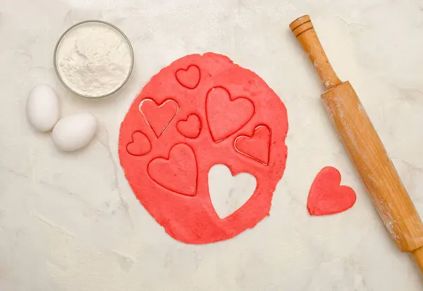 Bir oklava ve beyaz bir tablo, yumurta, yakın çekim kalpleri dışarı kesim ile kırmızı hamur — Stok fotoğraf