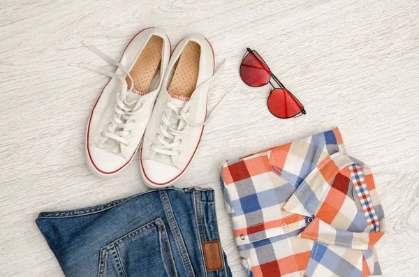 Camisa quadriculada brilhante, óculos, tênis e jeans. Fundo de madeira. Conceito na moda — Fotografia de Stock