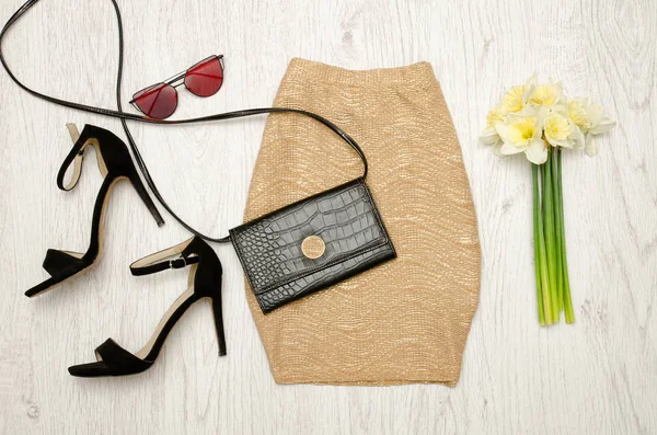 Falda dorada, zapatos, embrague, gafas y un ramo de narcisos. Concepto de moda. Fondo de madera . — Foto de Stock