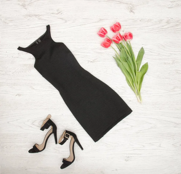 Zwarte vrouwelijke kleding, schoenen en roze tulpen op een houten achtergrond. Modieuze concept, bovenaanzicht — Stockfoto