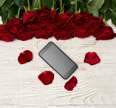 Smartphone, kırmızı gül ve yaprakları hafif ahşap zemin, üstten görünüm