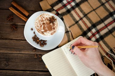 Bir kafede planlama. Kupa latte, içinde a defter bir kalem ile yazılı bir el. Üstten Görünüm