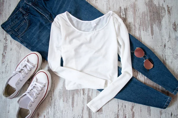 Camisola branca, jeans, tênis e óculos em um fundo de madeira. Conceito na moda, vista superior — Fotografia de Stock