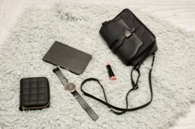 Siyah çanta, defter, saat, çanta ve ruj. Arka plan, üstten görünüm üzerinde beyaz kürk. moda kavramı