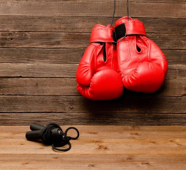 İki kırmızı boks eldivenleri bir tahta kahverengi zemin, ip atlama asılı — Stok fotoğraf